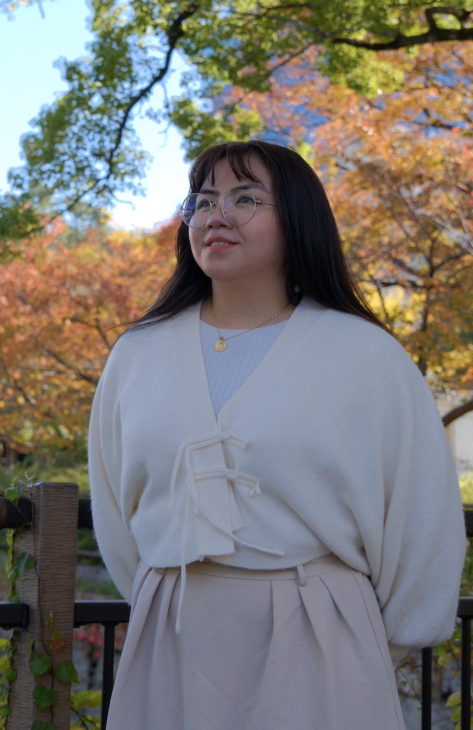 Sam in a cream cardigan among autumn foliage